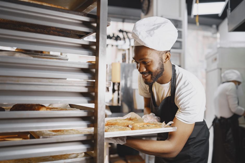 Baker in a kitchen holding a tray of fresh bread